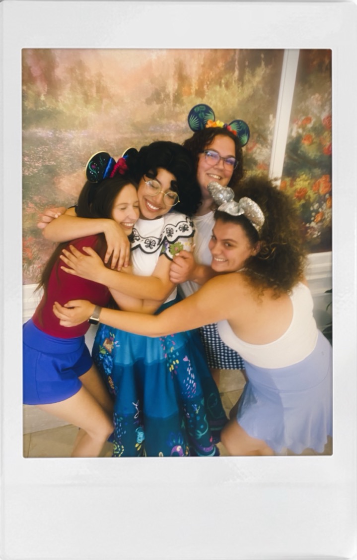 A polaroid of Beth Anderson and three castmates in a laughing group hug, wearing Disney ears