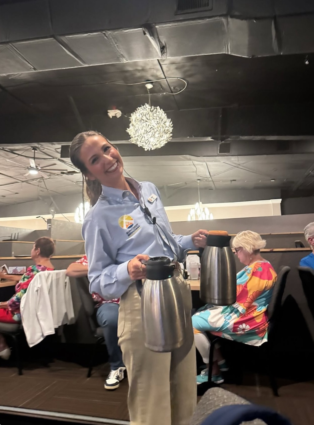 Beth Anderson laughing in her Suncoast Broadway uniform, carrying two coffee carafes through the dining room during dinner service